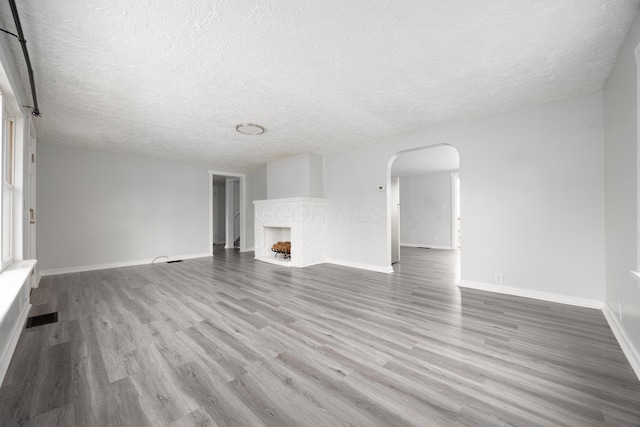 unfurnished living room featuring arched walkways, a fireplace, visible vents, wood finished floors, and baseboards