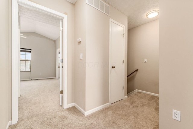 hall featuring carpet floors, visible vents, vaulted ceiling, a textured ceiling, and an upstairs landing