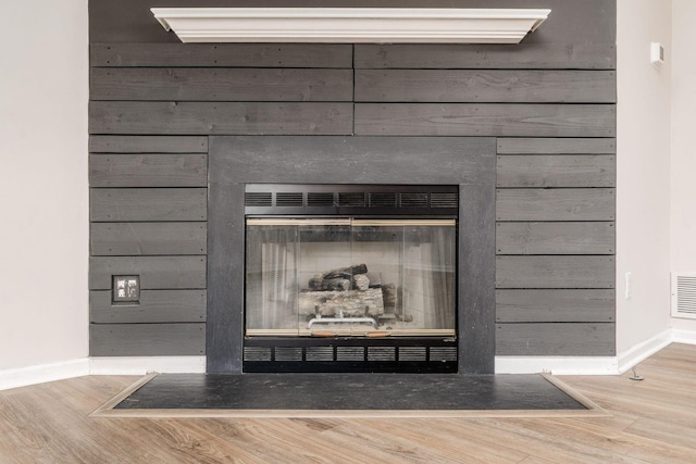 interior details featuring a glass covered fireplace, visible vents, baseboards, and wood finished floors