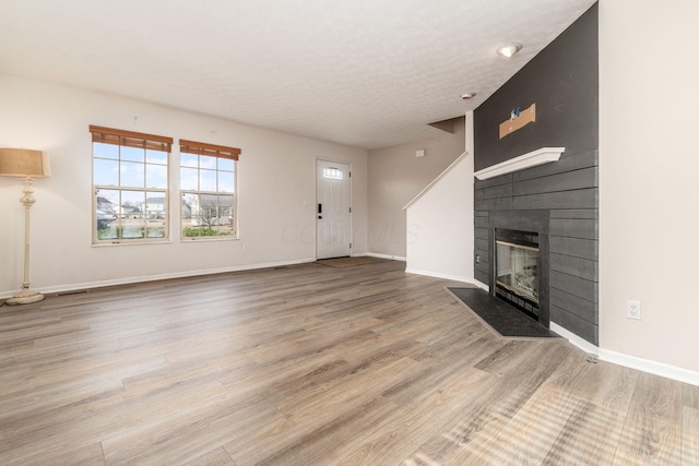 unfurnished living room with a textured ceiling, a fireplace, baseboards, and wood finished floors