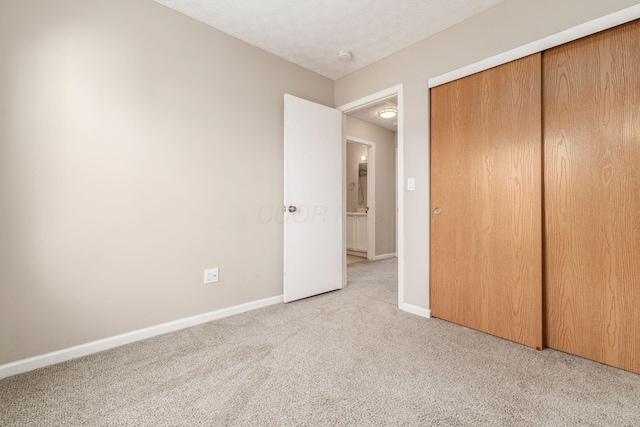 unfurnished bedroom featuring a closet, light colored carpet, a textured ceiling, and baseboards