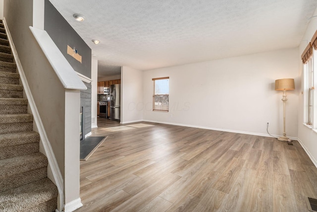 unfurnished living room featuring a textured ceiling, stairs, baseboards, and wood finished floors