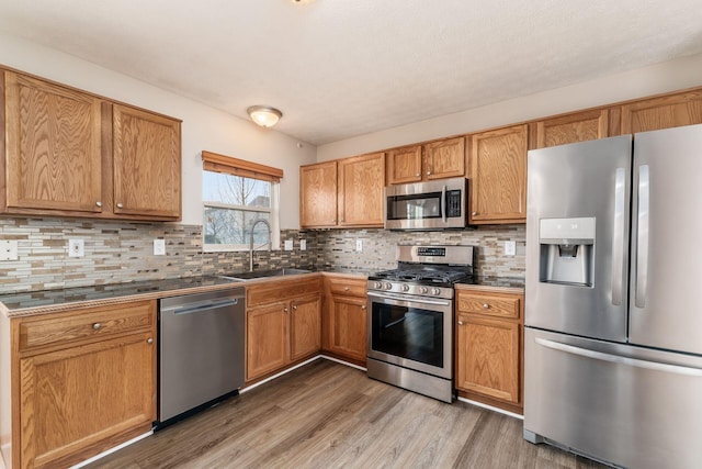 kitchen with stainless steel appliances, dark countertops, decorative backsplash, light wood-style floors, and a sink