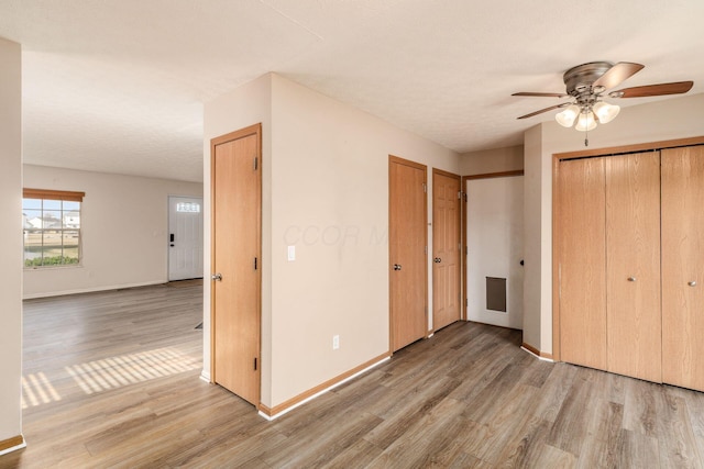 unfurnished bedroom with a textured ceiling, light wood-style flooring, a ceiling fan, baseboards, and two closets