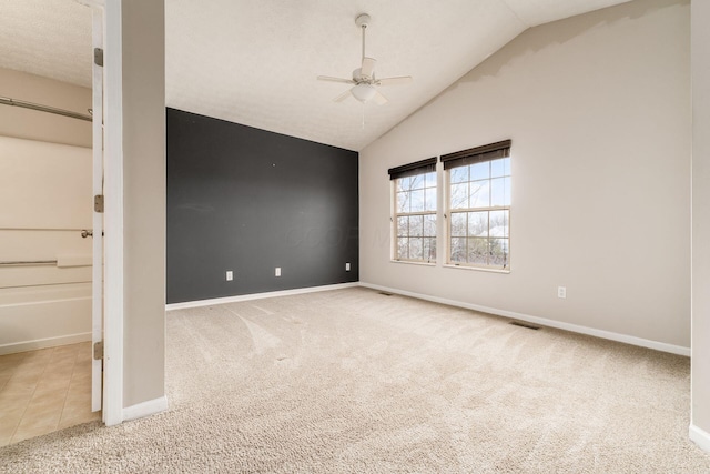 tiled spare room featuring visible vents, baseboards, lofted ceiling, ceiling fan, and carpet