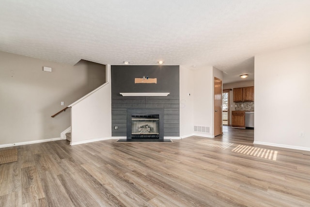 unfurnished living room with stairway, a large fireplace, visible vents, and light wood-style flooring