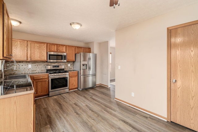 kitchen with a sink, stainless steel appliances, wood finished floors, and backsplash