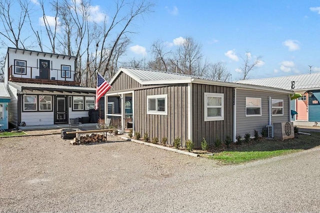 view of front of property with a balcony, metal roof, gravel driveway, ac unit, and board and batten siding