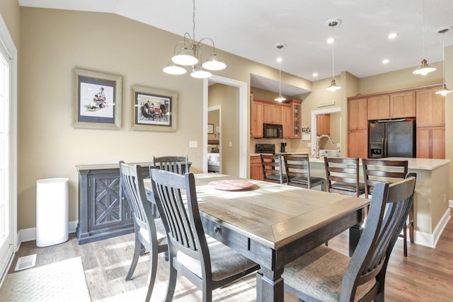 dining room with light wood-style floors, visible vents, vaulted ceiling, and baseboards