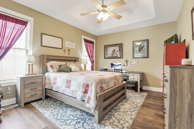 bedroom featuring a raised ceiling, visible vents, ceiling fan, wood finished floors, and baseboards