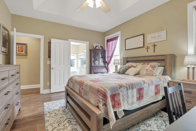 bedroom featuring ceiling fan, baseboards, a raised ceiling, and wood finished floors