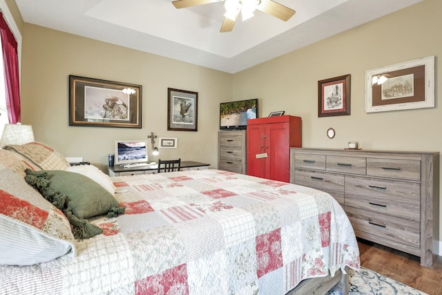 bedroom with a tray ceiling, wood finished floors, and a ceiling fan