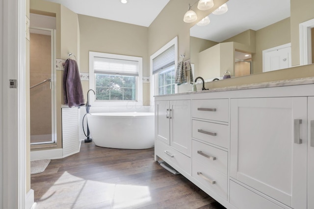 bathroom with double vanity, a stall shower, a soaking tub, and wood finished floors