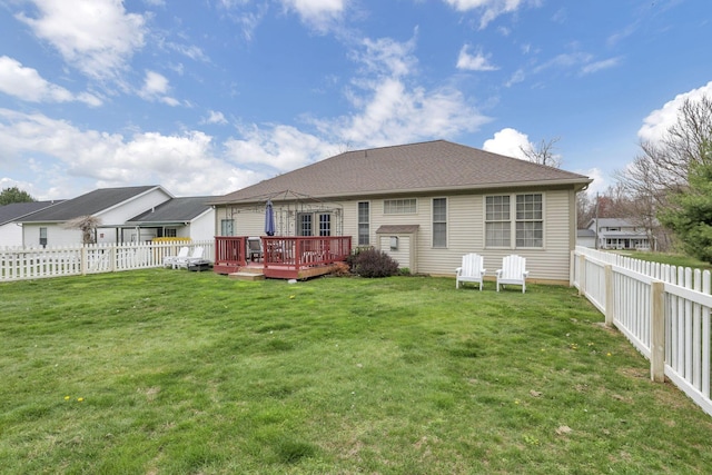 back of property with a shingled roof, a fenced backyard, a wooden deck, and a lawn