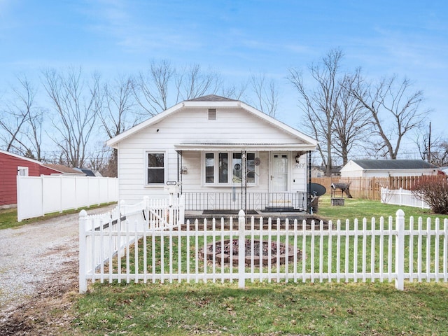 bungalow-style house featuring covered porch, driveway, a front lawn, and a fenced front yard