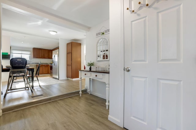 kitchen featuring light wood-type flooring, brown cabinetry, stainless steel refrigerator with ice dispenser, and baseboards