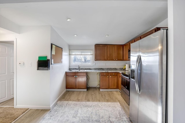 kitchen with brown cabinets, stainless steel appliances, light countertops, light wood-style floors, and a sink