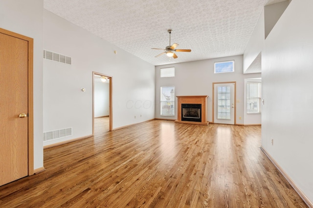 unfurnished living room featuring light wood-style floors, visible vents, a fireplace with raised hearth, and a ceiling fan