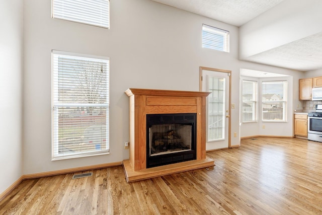 unfurnished living room with a fireplace with raised hearth, a textured ceiling, light wood-style flooring, visible vents, and baseboards