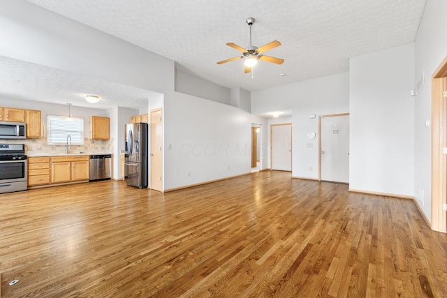 unfurnished living room featuring ceiling fan, a textured ceiling, a sink, and light wood-style flooring