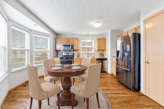 dining room featuring a wealth of natural light, baseboards, a textured ceiling, and light wood finished floors