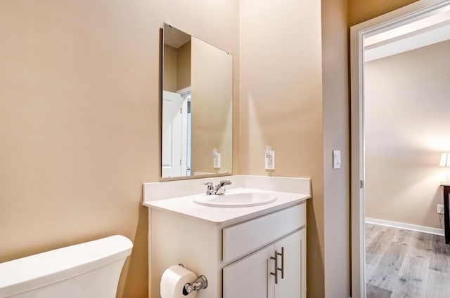 half bath with baseboards, vanity, toilet, and wood finished floors