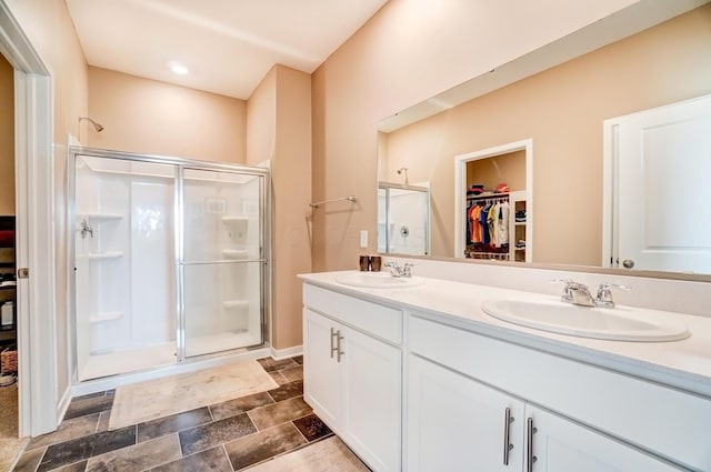 bathroom featuring a spacious closet, double vanity, a sink, and a shower stall