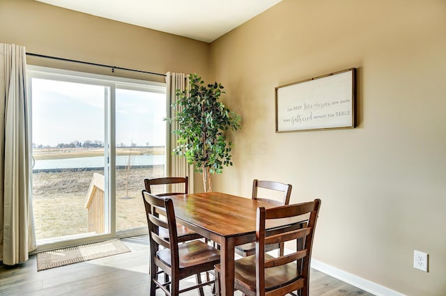 dining space featuring a water view, baseboards, and wood finished floors