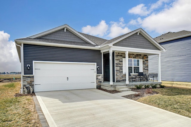 view of front of property with roof with shingles, a porch, an attached garage, stone siding, and driveway