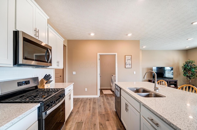 kitchen with a sink, appliances with stainless steel finishes, independent washer and dryer, light wood-type flooring, and light stone countertops