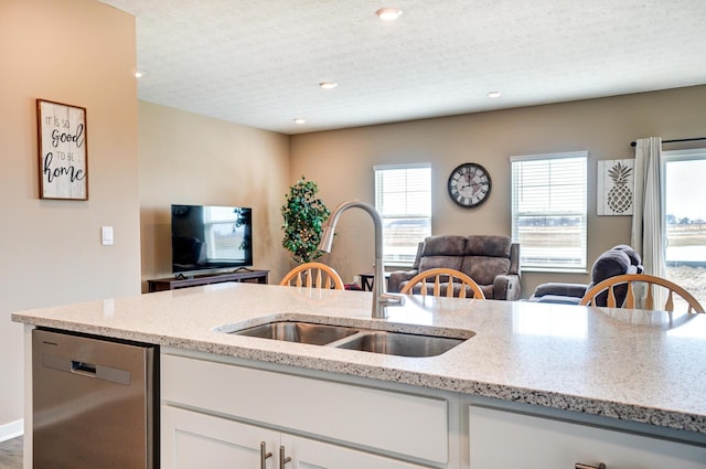 kitchen featuring light stone counters, open floor plan, dishwasher, and a sink