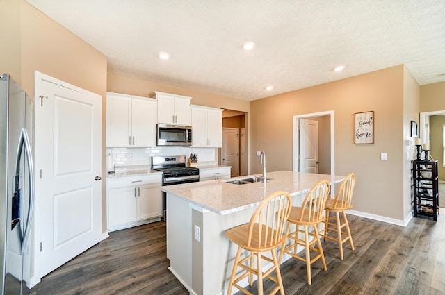 kitchen featuring dark wood-style flooring, a sink, a kitchen island with sink, stainless steel appliances, and backsplash