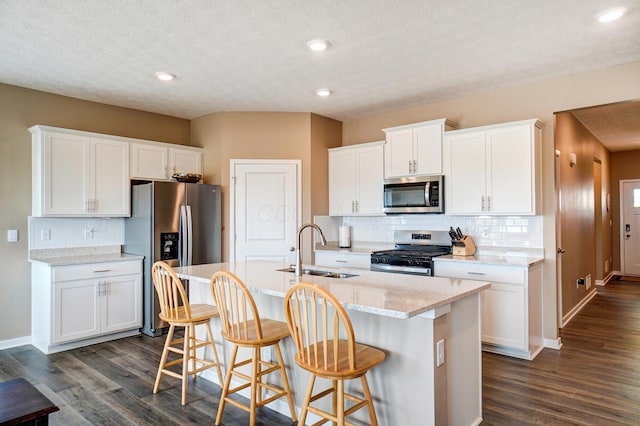 kitchen featuring stainless steel appliances, dark wood-style flooring, a kitchen island with sink, and a sink