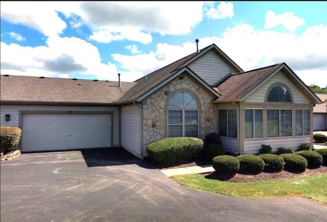 ranch-style house with a garage, stone siding, driveway, and a shingled roof