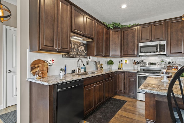 kitchen with stainless steel appliances, dark wood-style flooring, a sink, dark brown cabinets, and light stone countertops