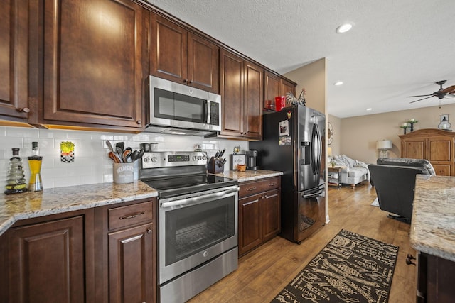 kitchen with stainless steel appliances, wood finished floors, backsplash, open floor plan, and light stone countertops