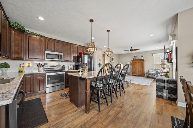 kitchen featuring stainless steel appliances, open floor plan, a kitchen island with sink, light wood-type flooring, and a kitchen breakfast bar