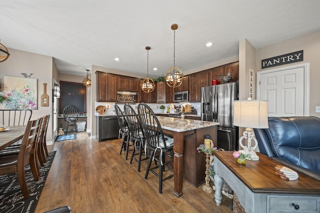 kitchen with a center island, dark wood-style flooring, pendant lighting, appliances with stainless steel finishes, and a kitchen bar