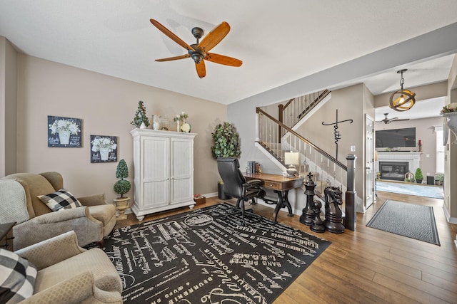 living room with stairs, ceiling fan, hardwood / wood-style floors, and a glass covered fireplace