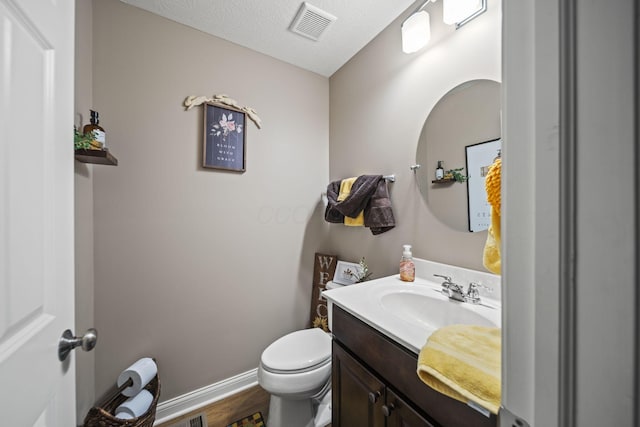 bathroom with visible vents, toilet, vanity, a textured ceiling, and baseboards