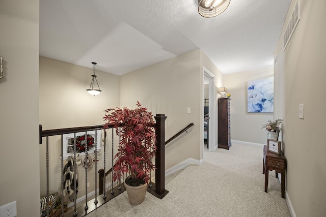 corridor with baseboards, visible vents, a textured ceiling, an upstairs landing, and carpet floors