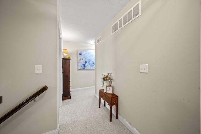 hall featuring light carpet, baseboards, visible vents, and an upstairs landing