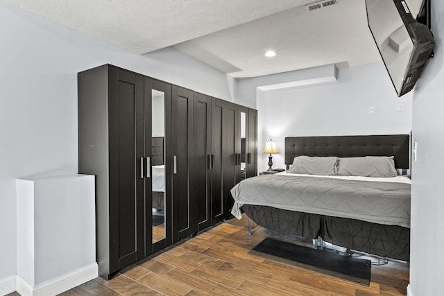 bedroom with a textured ceiling, recessed lighting, wood finished floors, visible vents, and baseboards