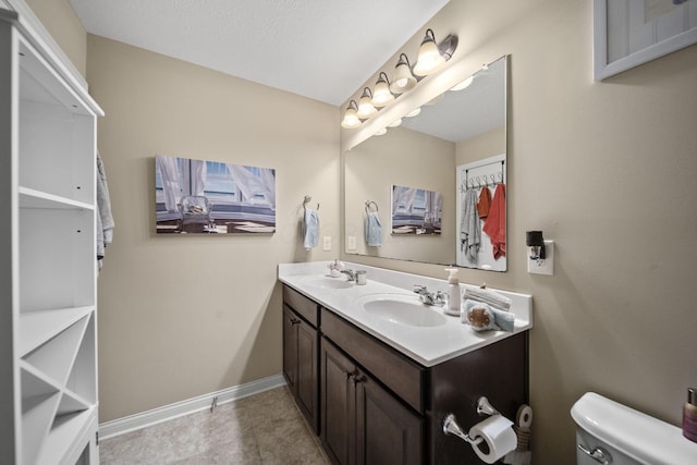 full bathroom with toilet, double vanity, baseboards, and a sink