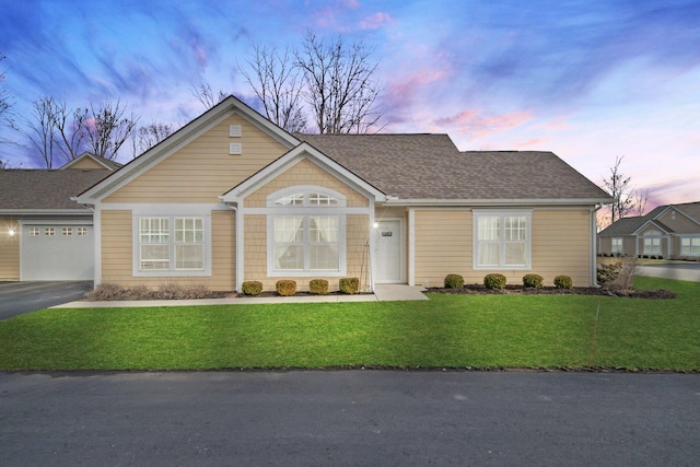 ranch-style home with a garage, driveway, a lawn, and roof with shingles