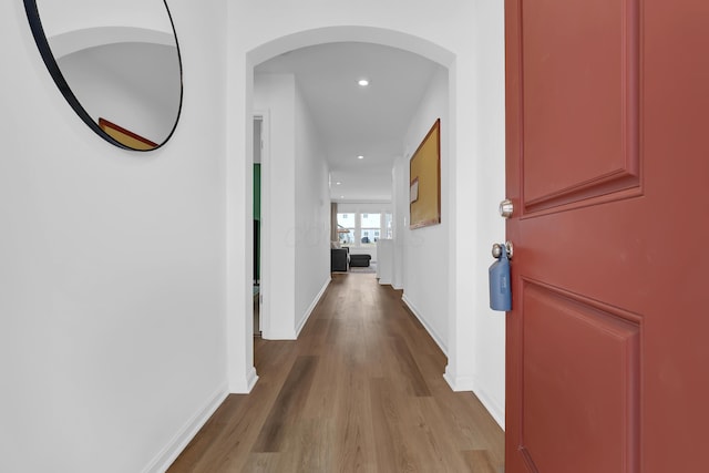 corridor with baseboards, arched walkways, wood finished floors, and recessed lighting