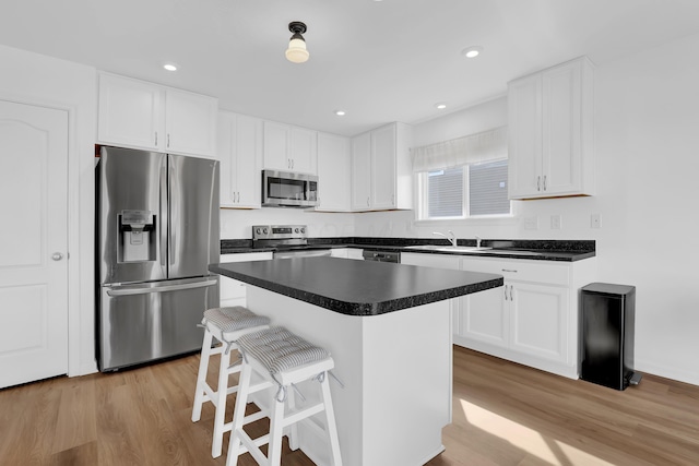 kitchen featuring white cabinets, dark countertops, appliances with stainless steel finishes, light wood-type flooring, and a sink