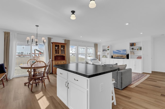 kitchen featuring light wood finished floors, dark countertops, an inviting chandelier, white cabinetry, and a kitchen island