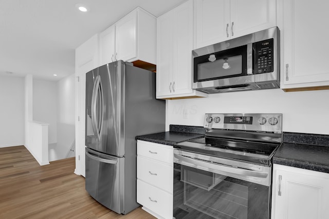 kitchen with stainless steel appliances, dark countertops, white cabinetry, and light wood-style floors