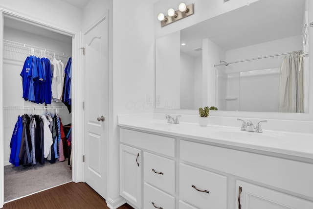 full bathroom featuring a sink, wood finished floors, a shower with curtain, double vanity, and a walk in closet